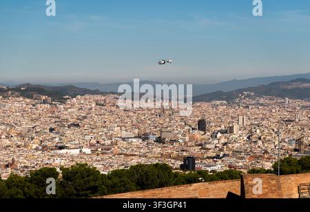 Luftbild der weitläufigen Stadtlandschaft von Barcelona mit einem Hubschrauber, der über dichten städtischen Gebäuden und fernen Bergen unter einem klaren blauen Himmel fliegt i Stockfoto