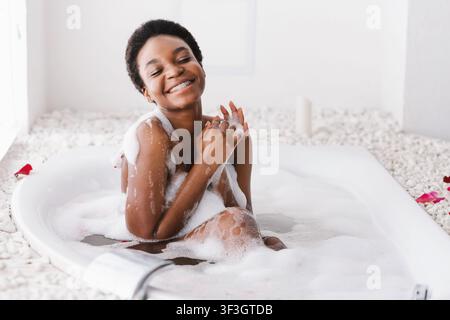 Frau mit geschlossenen Augen des Vergnügens Baden mit Schaum Und Blütenblätter zu Hause Stockfoto