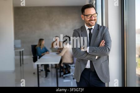 Gutaussehender junger Geschäftsmann, der vor seinem Team selbstbewusst im Firmenbüro steht Stockfoto