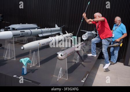 Reinigungskräfte fegen Staub von einer Ausstellung verschiedener Raketensysteme, darunter METEOR, ASRAAM, SPEAR und AKERON, die auf dem MBDA-Stand auf der Farnborough International Air Show am 23. Juli 2026 in Farnborough, England, gezeigt werden. Das in Frankreich ansässige MBDA ist ein europäischer multinationaler Entwickler und Hersteller von Raketen. Es wurde im Dezember 2001 nach der Fusion der wichtigsten französischen, britischen und italienischen Raketensysteme gegründet; Matra, BAe Dynamics und Alenia. Farnborough International ist eine 500.000 qm große Handels- und Industrieausstellung für Luftfahrt, Verteidigung und Luft- und Raumfahrt. Insgesamt werden 103 statische und Ausstellungsflugzeuge gezeigt Stockfoto