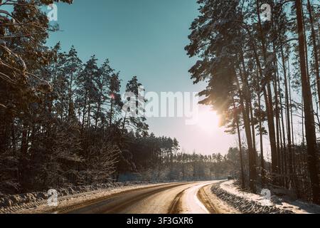 Gebogene schneebedeckte Straße durch einen sonnigen Winterwald in Europa. Stockfoto