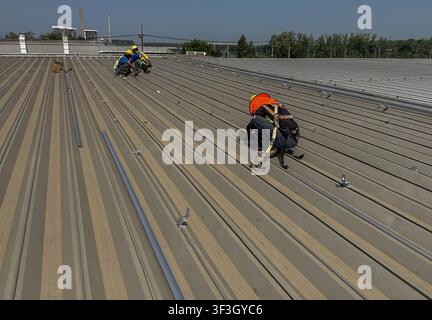 Nahaufnahme von photovoltaischen Solarpanelen, die auf einem Metalldach einer Industrieanlage installiert sind, mit Montageschienen und Erdungsbauteilen für erneuerbare Energien Stockfoto