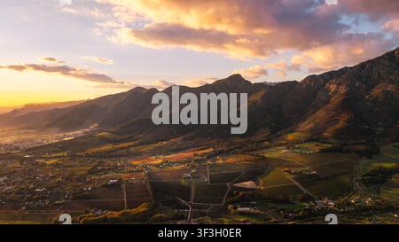 Luftbild des Franschhoek-Tals mit üppigen Weinbergen, sanften Hügeln und dramatischen Bergen im warmen Glanz der goldenen Stunde in Franschhoek Stockfoto