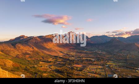 Luftbild des Franschhoek-Tals mit seinen üppigen Weinbergen und dramatischen Bergketten, die vom warmen Schein des Sonnenuntergangs in Franschhoek, West, beleuchtet werden Stockfoto