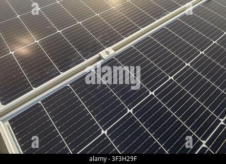 Nahaufnahme von photovoltaischen Solarpanelen, die auf einem Metalldach einer Industrieanlage installiert sind, mit Montageschienen und Erdungsbauteilen für erneuerbare Energien Stockfoto