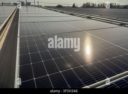 Nahaufnahme von photovoltaischen Solarpanelen, die auf einem Metalldach einer Industrieanlage installiert sind, mit Montageschienen und Erdungsbauteilen für erneuerbare Energien Stockfoto