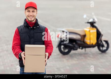 Fröhlicher Fahrer Hält Boxen Und Lächelnd In Der Nähe Des Motorrads In Der Stadt Stockfoto