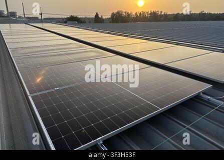 Nahaufnahme von photovoltaischen Solarpanelen, die auf einem Metalldach einer Industrieanlage installiert sind, mit Montageschienen und Erdungsbauteilen für erneuerbare Energien Stockfoto