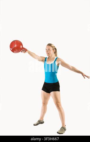 Sportliche Frau, die einen Arm beim Kettlebell-Schwingen ausstreckt, während sie die Haltung hält Stockfoto