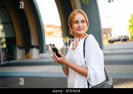 Lächelnde Frau hält Smartphone in der Stadt bei Sonnenuntergang Stockfoto