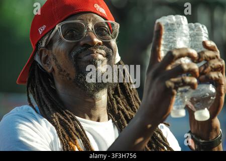 Mann mit Dreadlocks lächelt und hält Wasserflaschen Stockfoto