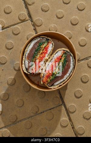 Sushi-Burger auf gelben texturierten Pflastersteinen. Lieferbox Stockfoto