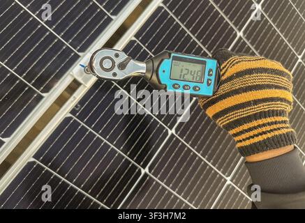 Nahaufnahme eines Technikers, der einen digitalen Drehmomentenschlüssel verwendet, um Verbindungselemente auf einem Photovoltaik-Solarmodul-Montagesystem auf dem Dach festzuziehen und zu überprüfen. Precisio Stockfoto