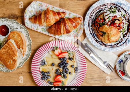 Eine Komposition mit verschiedenen Frühstücksartikeln auf Vintage-Tellern. Oberansicht. Pfannkuchen, Croissants, Eier, Toast, Käse, Saucen, Mozzarella, Kaffee, ein Stockfoto