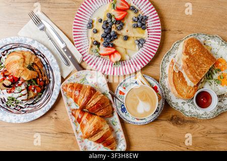 Eine Komposition mit verschiedenen Frühstücksartikeln auf Vintage-Tellern. Oberansicht. Pfannkuchen, Croissants, Eier, Toast, Käse, Saucen, Mozzarella, Kaffee, ein Stockfoto