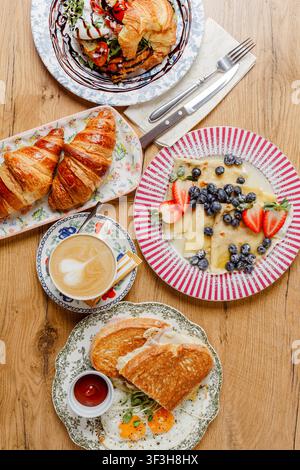 Eine Komposition mit verschiedenen Frühstücksartikeln auf Vintage-Tellern. Oberansicht. Pfannkuchen, Croissants, Eier, Toast, Käse, Saucen, Mozzarella, Kaffee, ein Stockfoto