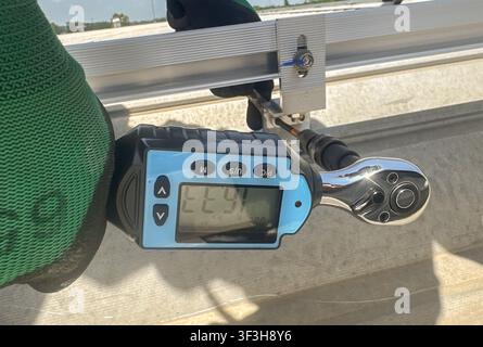 Nahaufnahme eines digitalen Drehmomentenschlüssels, der eine Schraube an einem Montageprofil für Photovoltaik-Solarpaneele während der Dachinstallation anzieht. Präzisions-Drehmomentmessung Stockfoto