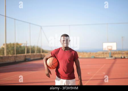 Junger schwarzer Mann lächelt auf einem Outdoor-Basketballplatz Stockfoto