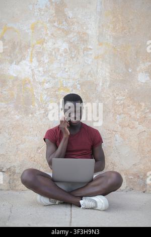 Junger Mann arbeitet remote mit Telefon und Laptop draußen Stockfoto