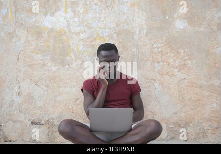 Junger schwarzer Mann arbeitet draußen mit Laptop und Handy Stockfoto
