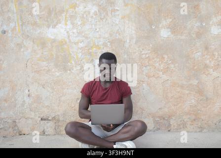 Junger Mann sitzt draußen mit Laptop und Ohrstöpseln Stockfoto