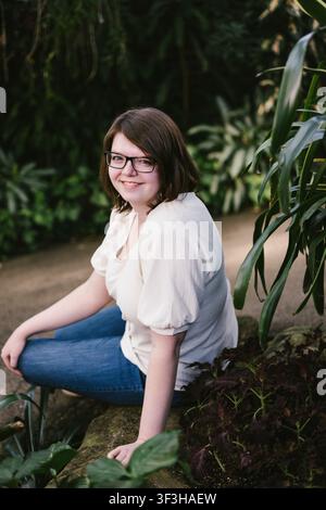 Junge Frau mit Brille lächelt in einem üppigen Garten Stockfoto
