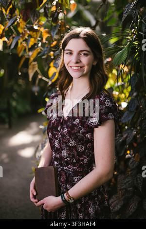 Fröhliche junge Frau hält ein Buch in einem Garten Stockfoto