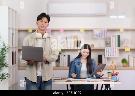 Lächelnder asiatischer Designer mit Laptop in einem Kreativstudio Stockfoto