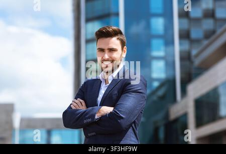 Schöner Geschäftsmann mit verschränkten Armen vor dem Bürogebäude Stockfoto