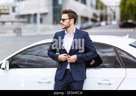 Kaukasischer Geschäftsmann in eleganten Anzug in der Nähe seines neuen Autos im Stadtzentrum stehen Stockfoto