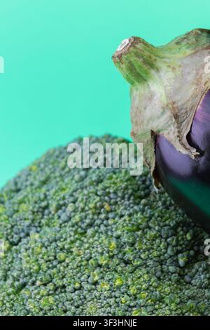 Eine vertikale Makrofotografie, die sich auf die kontrastierenden Texturen eines grünen Brokkolisprießes und der glatten Haut einer violetten Aubergine konzentriert. Das strahlende Grün Stockfoto