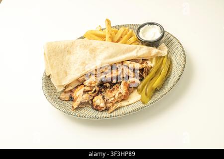 Gegrillter Hühner-Shawarma-Wrap offen auf einem Teller, serviert mit Pommes, Knoblauchsauce und Gurkenscheiben vor weißem Hintergrund. Stockfoto