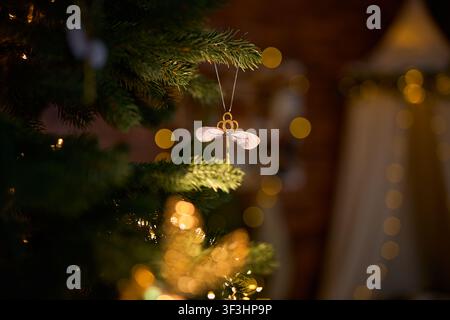 Ein vertikales Urlaubsfoto eines magischen fliegenden Schlüssel-Ornaments mit zarten Flügeln, das an einem immergrünen Weihnachtsbaum hängt, mit einem verträumten, sanft verschwommenen Hintergrund Stockfoto