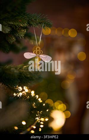 Ein vertikales Urlaubsfoto eines magischen fliegenden Schlüssel-Ornaments mit zarten Flügeln, das an einem immergrünen Weihnachtsbaum hängt, mit einem verträumten, sanft verschwommenen Hintergrund Stockfoto