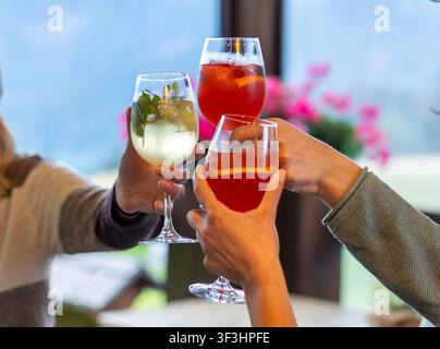 Gruppe von Freunden, die mit Gläsern anstoßen, die Aperitivo-Getränke in verschiedenen Farben enthalten: weißer Spritz wie Hugo und Holunderblüten-Spritz sowie roter Coc Stockfoto