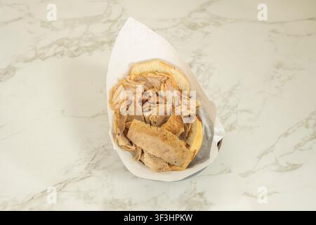 "Gemischtes Doner-Kapsalon-Sandwich in Papier eingewickelt auf weißer Marmor-Arbeitsplatte" Stockfoto