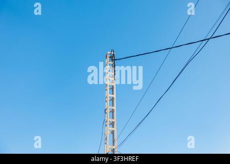 Beton-Nutzmast mit Überhead-Kabeln vor blauem Himmel Stockfoto