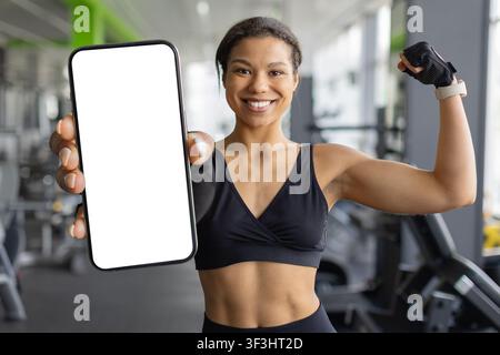 Lächelnde junge schwarze Frau hält ein leeres Smartphone und spannt ihren Arm Stockfoto