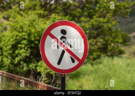 Rundes Verkehrsschild mit rotem Rand und diagonaler Linie über einem schwarzen Fußgänger-Symbol, das einen gesperrten oder unsicheren Gehbereich anzeigt Stockfoto