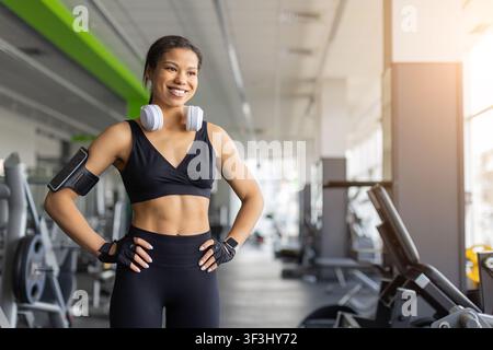 Selbstbewusste schwarze Frau in Sportkleidung steht mit den Händen in die Hüften gestemmt im Fitnessstudio Stockfoto