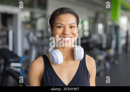 Lächelnde schwarze Frau, die nach dem Training weiße kabellose Kopfhörer um den Hals trägt Stockfoto