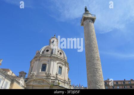 Ein sonniger Tagesblick auf die historische Trajanssäule neben der Kirche des Allerheiligsten Namens Maria im Trajanforum in Rom. Stockfoto