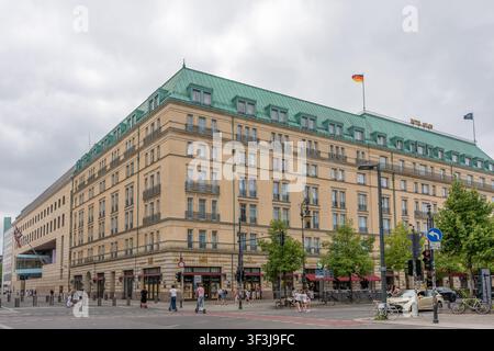 Berlin, Deutschland, 18. Juli 2026. Ein weiter Straßenblick zeigt das Hotel Adlon Kempinski unter grauen Sommerwolken. Die deutsche Flagge und das grüne Kupferdach dominieren Stockfoto