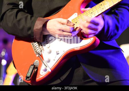 Nahaufnahme eines E-Gitarristen, der live auf der Bühne mit einer roten Stratocaster-Gitarre unter farbenfroher Konzertbeleuchtung spielt. Stockfoto