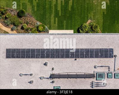Luftbild einer Reihe von Solarpanelen, die auf einem Flachdach mit angrenzendem Grünstreifen und Gartengebiet in Cascais, Lisboa, Portugal, installiert sind. Stockfoto