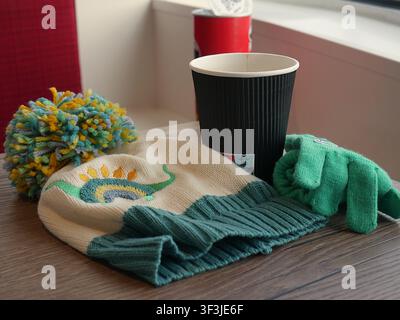 Ein dekorativer blauer Keramikübertopf mit lebhaftem grünem Laub, gepaart mit einer passenden Tasse auf einer rustikalen Kante vor neutraler Wandkulisse. Stockfoto
