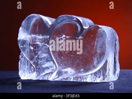 Zwei Herzen aus einem Steinsalz-Kristall. Statuette mit Herzen auf rotem Hintergrund. Zwei transparente Herzen. Stockfoto