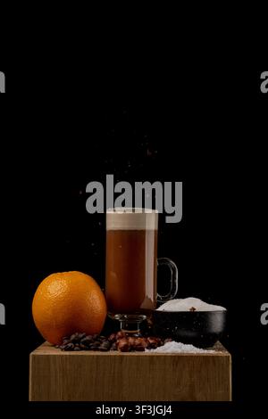 Ansicht eines Kaffeedrinkes in einem Glas mit einer Orange, Kaffeebohnen, Haselnüssen und Zucker auf einem Holzblock in Norwegen. Stockfoto