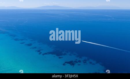 Possidi Beach, Griechenland 11. Juli 2026. Eine Drohnenaufnahme zeigt ein kleines Boot, das durch die klaren blauen Gewässer vor Possidi Beach in Griechenland fährt an einem su Stockfoto