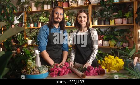 Porträt eines erfolgreichen, glücklichen erwachsenen Mannes und einer hübschen, bezaubernden jungen Floristin, die in die Kamera lächeln und einen Blumenstrauß im Blumenladen dekorieren Stockfoto